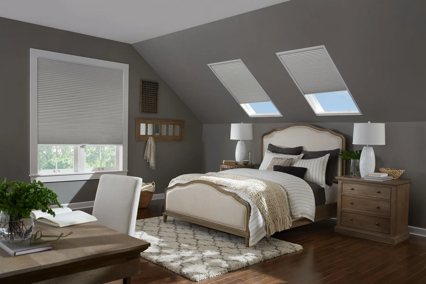Grey honeycomb shades on two angled skylights and a window in an attic bedroom.