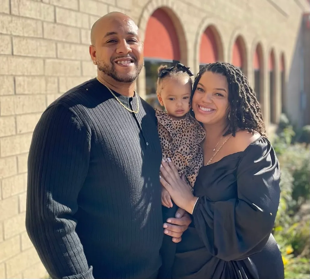 Josh and Shade’ standing outside in the sun with their young daughter held between them