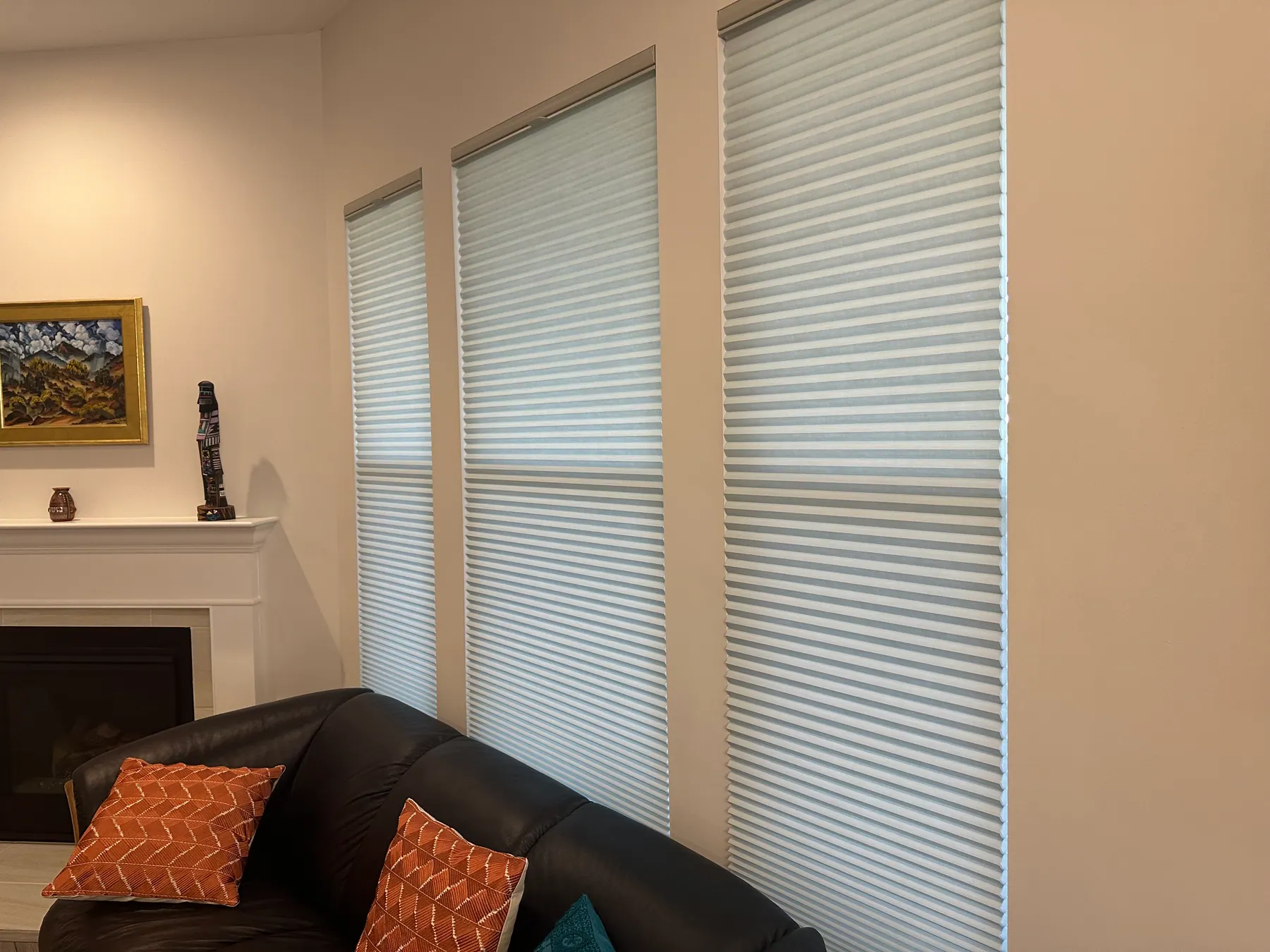 White cellular shades lowered on three tall windows beside a white fireplace in a living room.