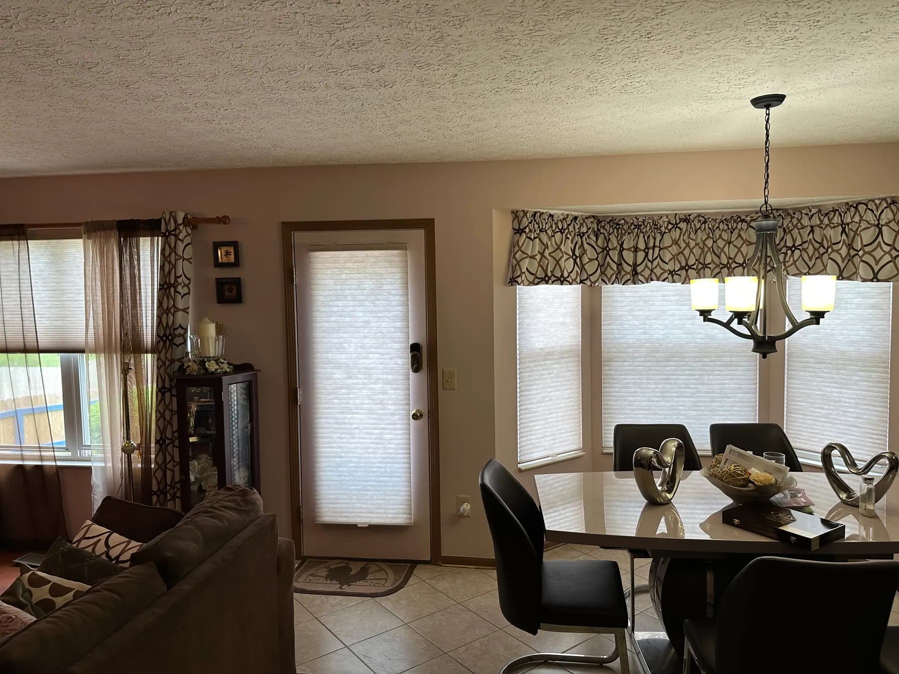 Cellular shades on a kitchen patio door and on the windows of a breakfast nook beneath a patterned valance.
