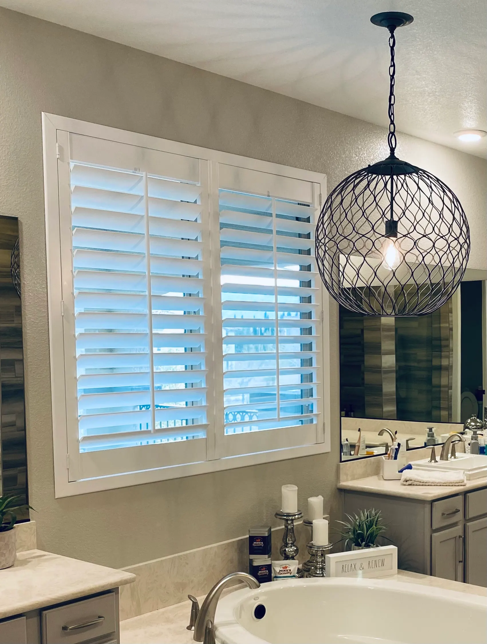 White plantation shutters with wide louvers on a primary bathroom window above a soaking tub.
