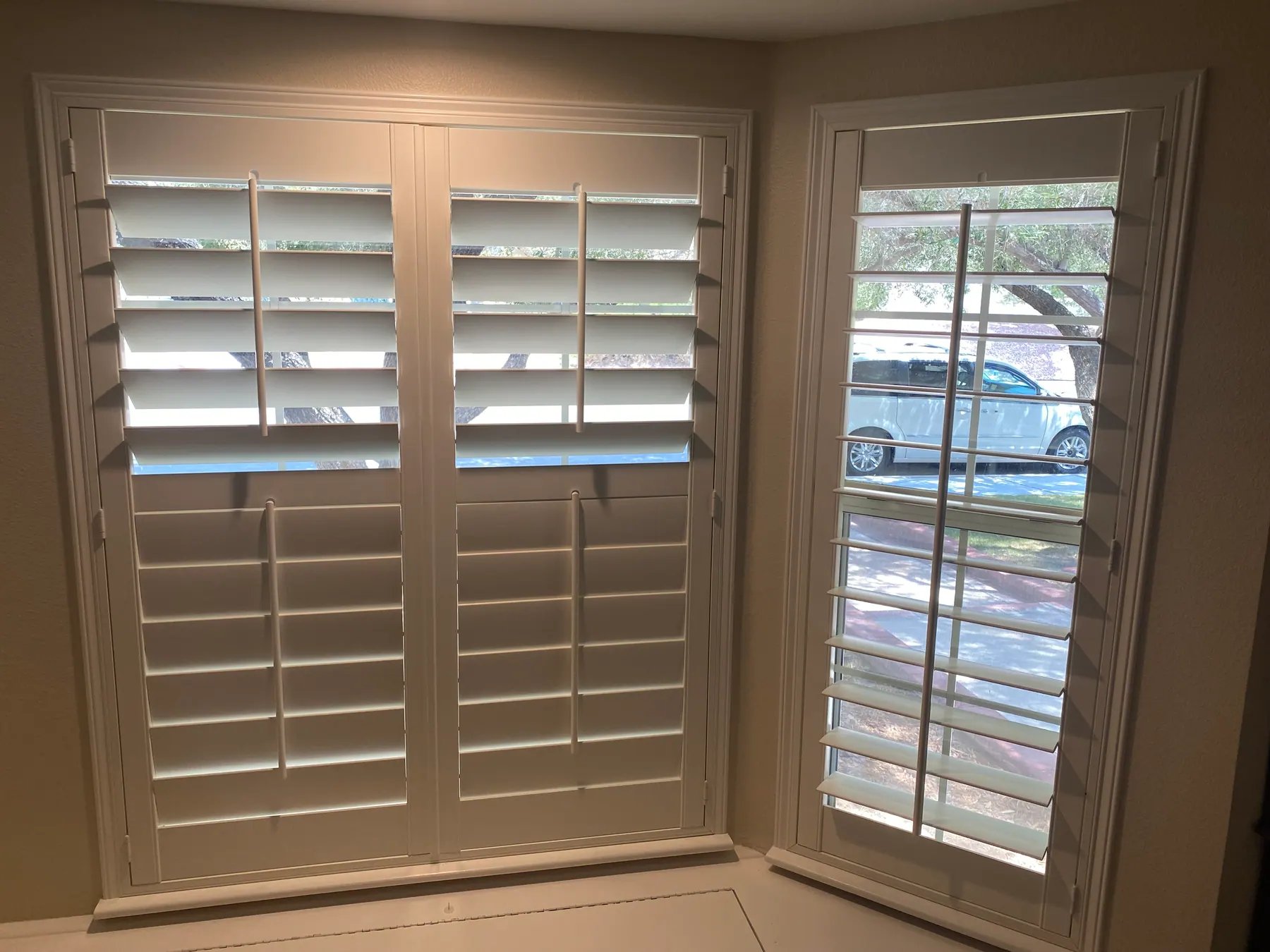 White plantation shutters mounted on a pair of French doors and on the tall window beside them.