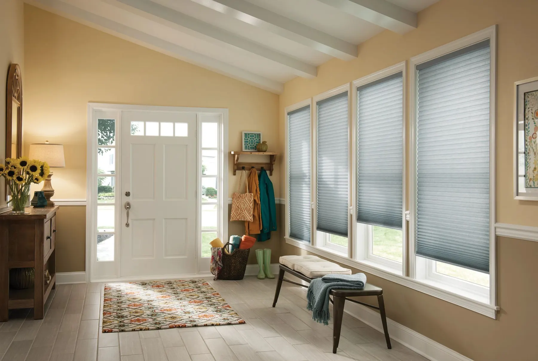 Blue-grey honeycomb shades on a row of tall windows beside a white front door in a sunny entryway.