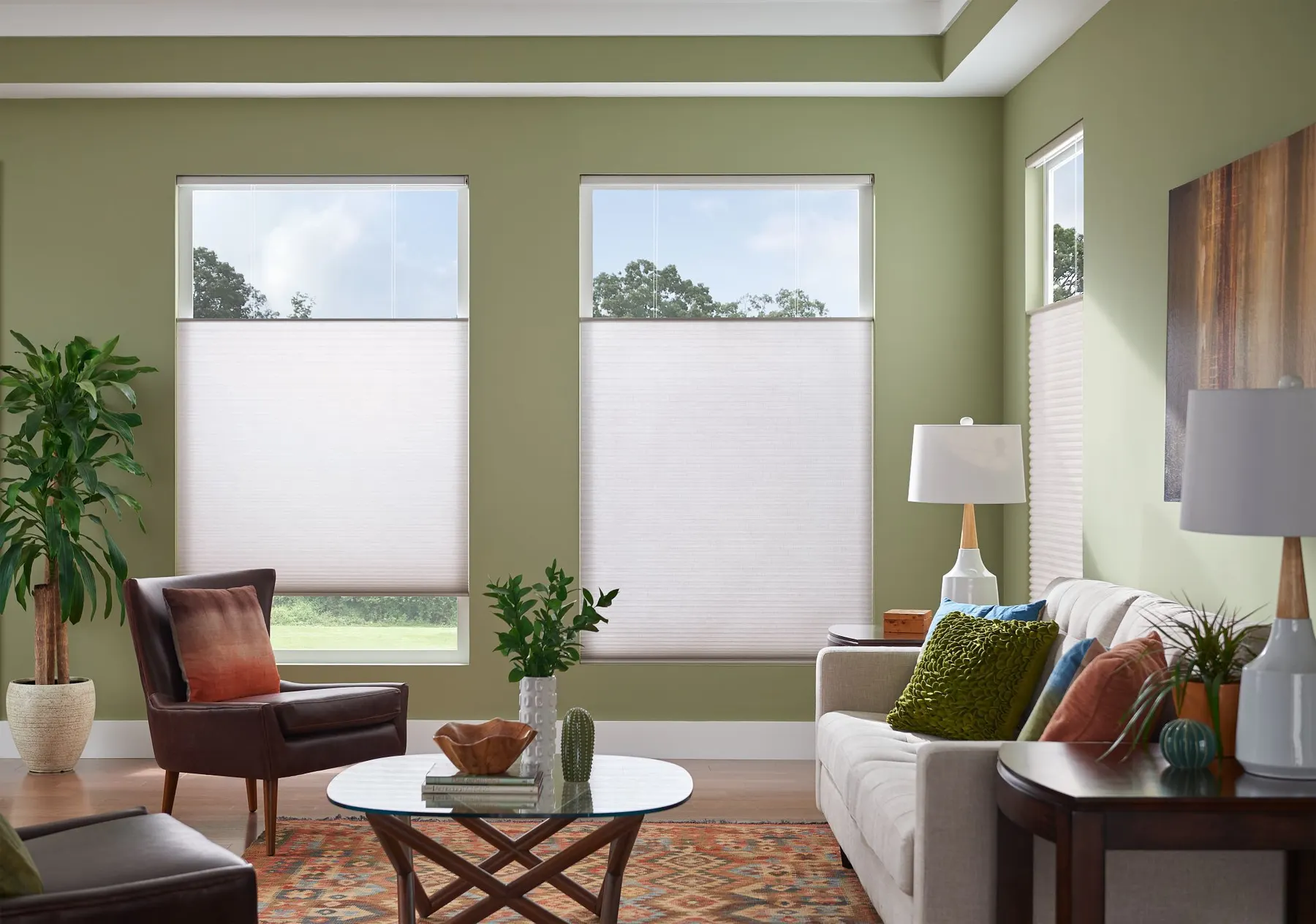 White top-down bottom-up honeycomb shades lowered from the top of two windows in a green living room, leaving the sky in view.