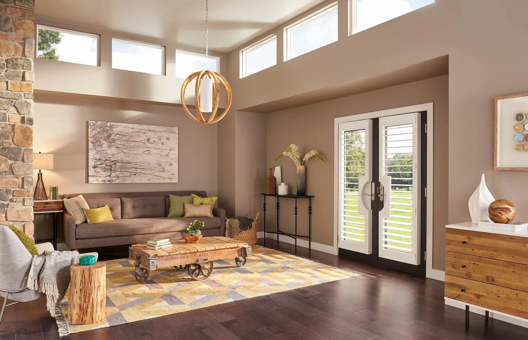 White shutters on a pair of French doors in a warm living room with clerestory windows and a stone wall.